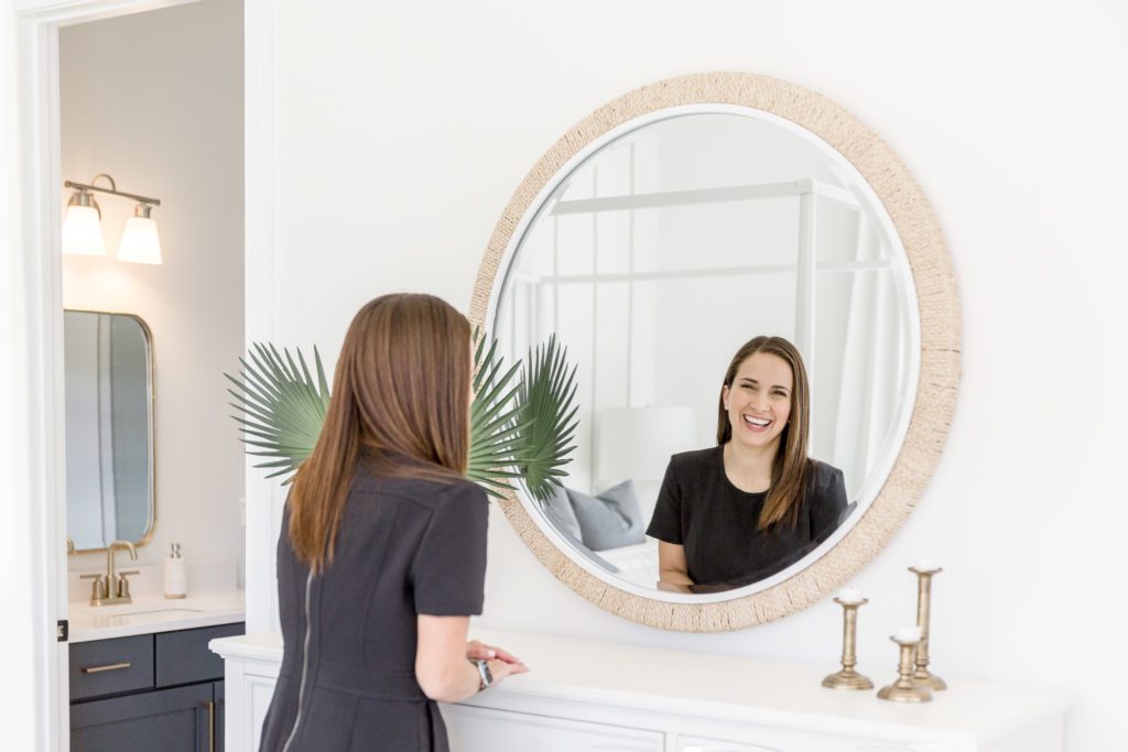 Luxury home real estate advisor smiling at a round mirror.