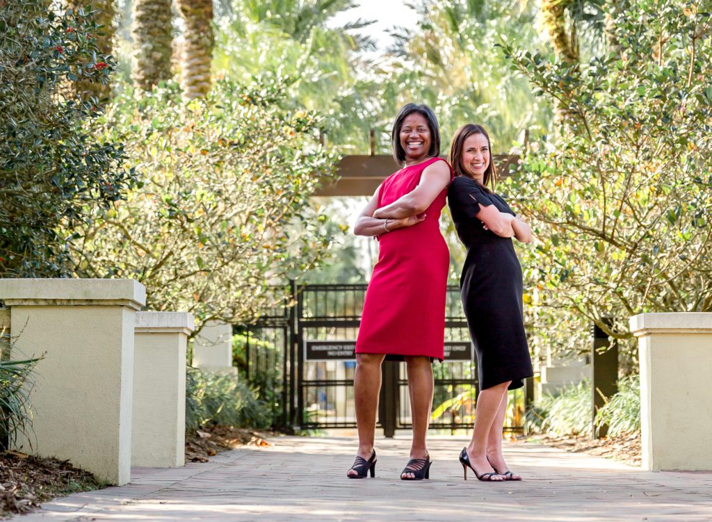 Two professional real estate advisors posing outside with trees in background.
